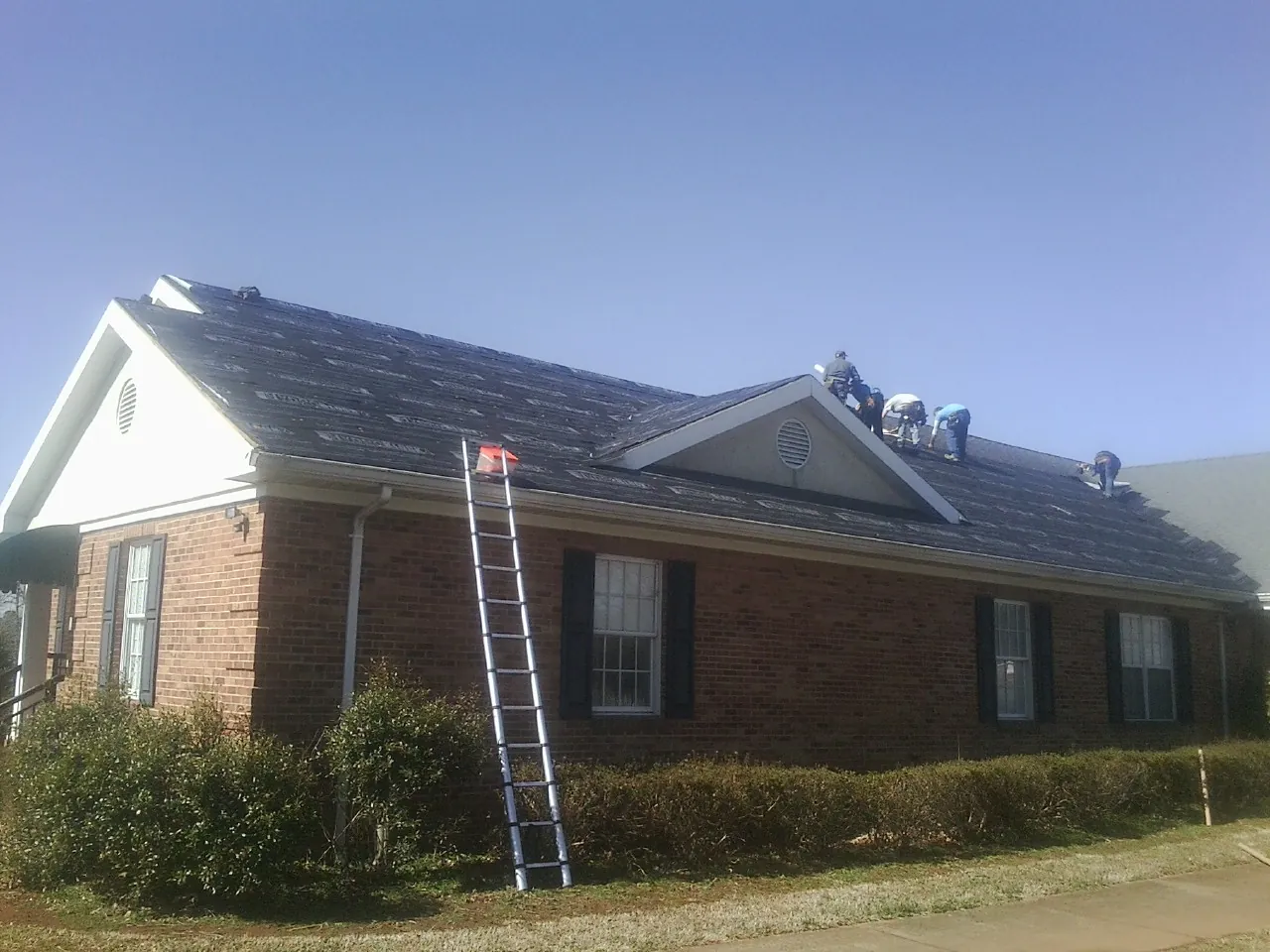 Crew tearing shingles off a brick ranch roof with a ladder set — Metal Roof Repair work by our crew in Guys Mills