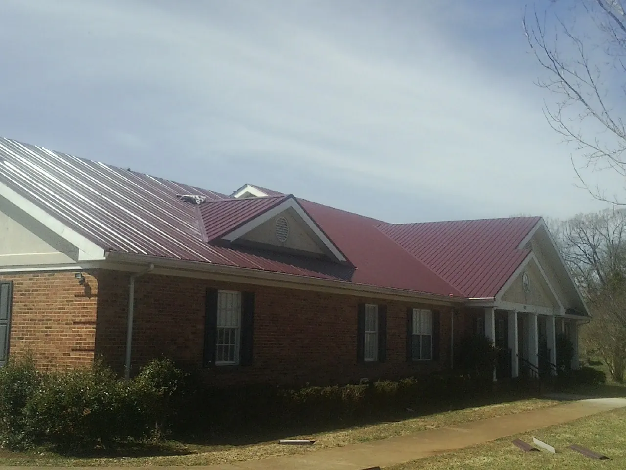 Red metal roof with gabled entries on a long brick building, from a Hail Damage Roof Repair job in Guys Mills