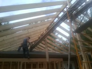 Rafters going up over a new addition with a worker on the wall in Guys Mills
