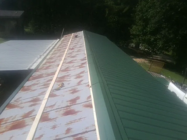 Old rusted panels beside newly installed green metal roofing — Wind Damage Roof Repair by Roofing Brothers in Guys Mills