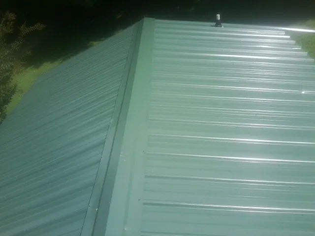 New green metal panels meeting at the ridge of a roof — Flat Roof Repair work by our crew in Guys Mills