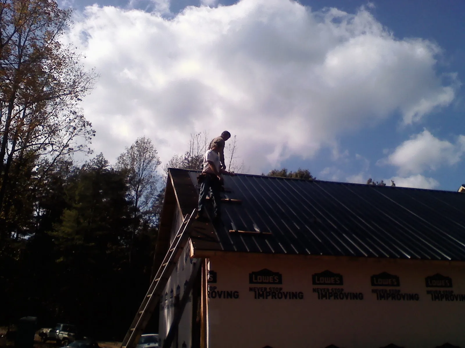 Roofer fastening dark metal panels high against a cloudy sky, from a Roof Inspection job in Guys Mills