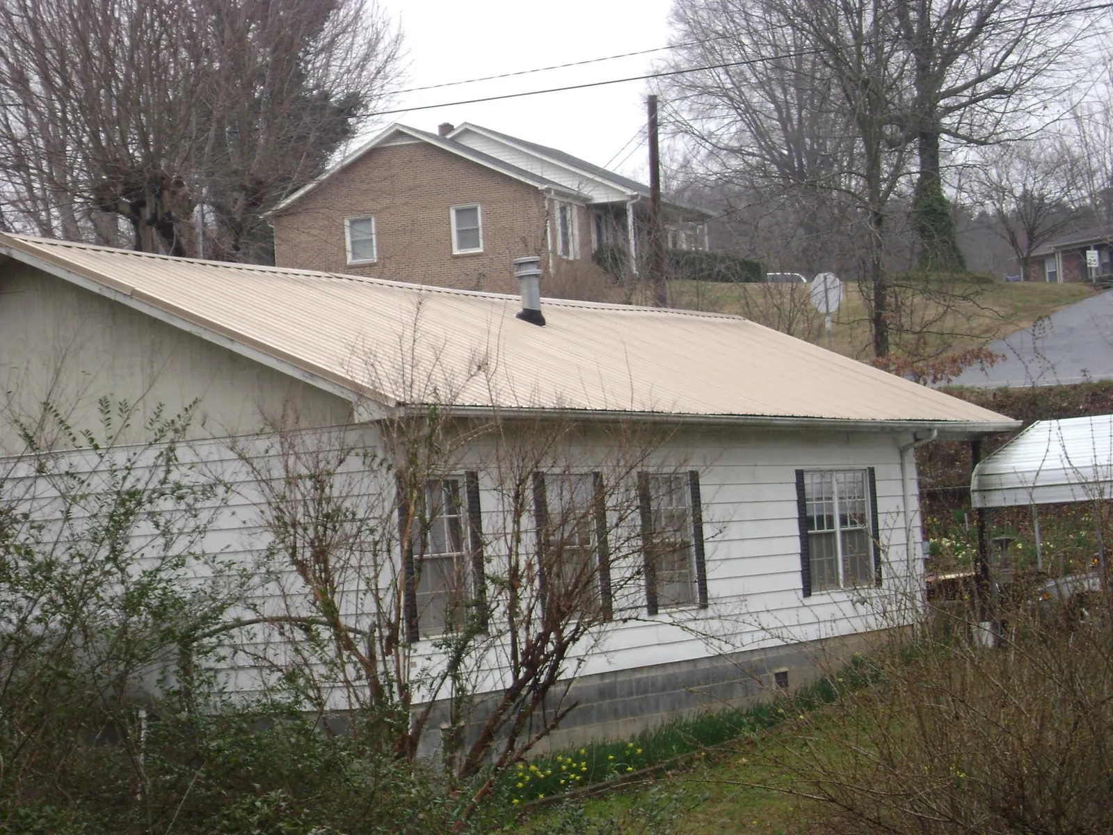 Tan metal roof on a white sided house set into a hillside — Commercial Roofing by Roofing Brothers in Guys Mills