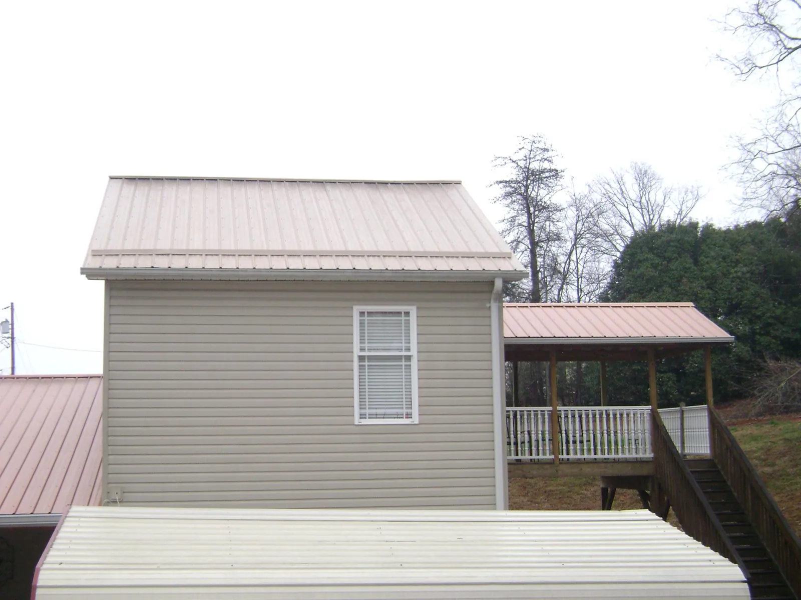Tan metal roofs on a two story addition and attached porch, from a Roof Replacement job in Guys Mills